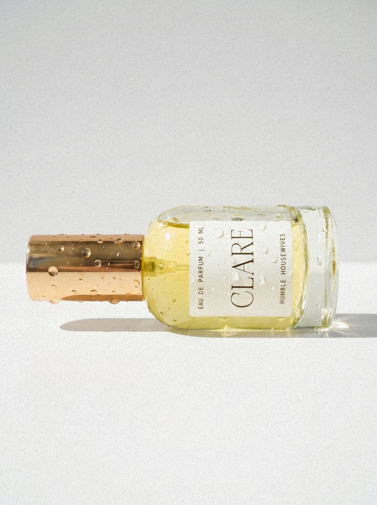 Clare Eau de Parfum lying on its side, bottle and gold cap beaded with water.