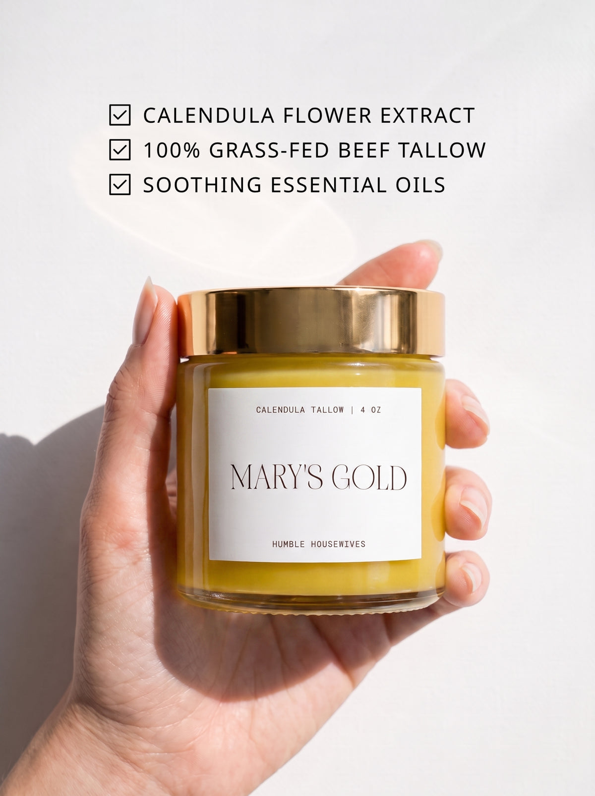 A hand holding the Mary's Gold Calendula Tallow jar. Text: calendula flower extract, 100% grass-fed beef tallow, soothing essential oils.